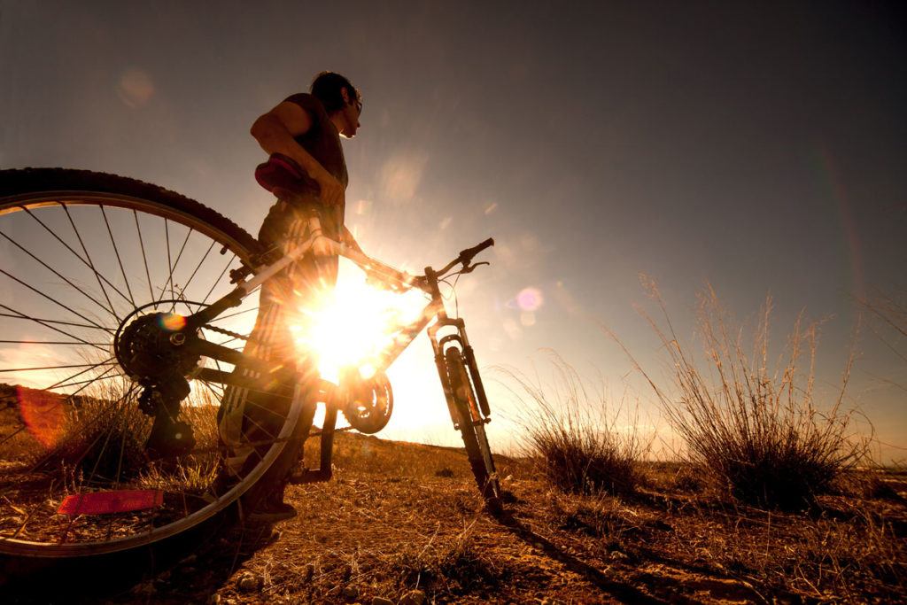 A cyclist standing by a bike with the low sun in the distance